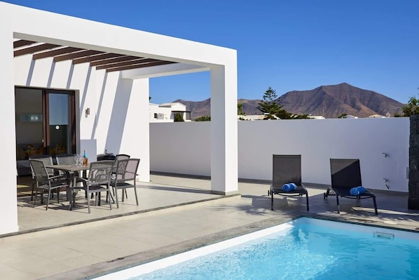 A modern outdoor pool area with a pergola, seating, and a mountain view.
