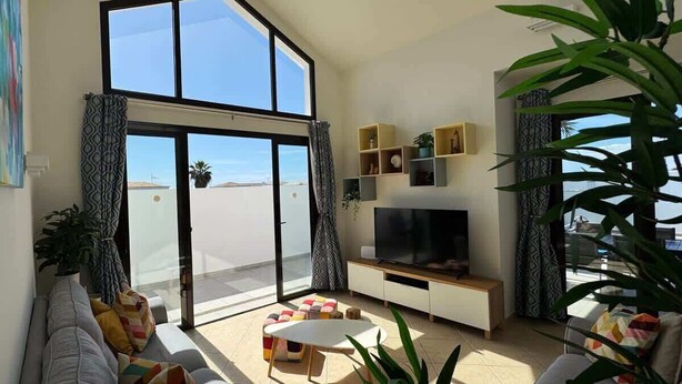 A modern living room with a large TV, a sofa, a coffee table, and a balcony with a view.
