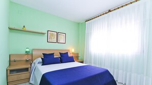 Une chambre d’hôtel comprenant un lit, des tables de chevet, une étagère avec des objets décoratifs et une fenêtre avec des rideaux légers.