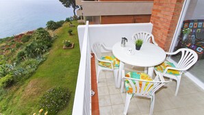 Un balcon avec une table et des chaises blanches, une plante en pot et une vue sur l’océan.