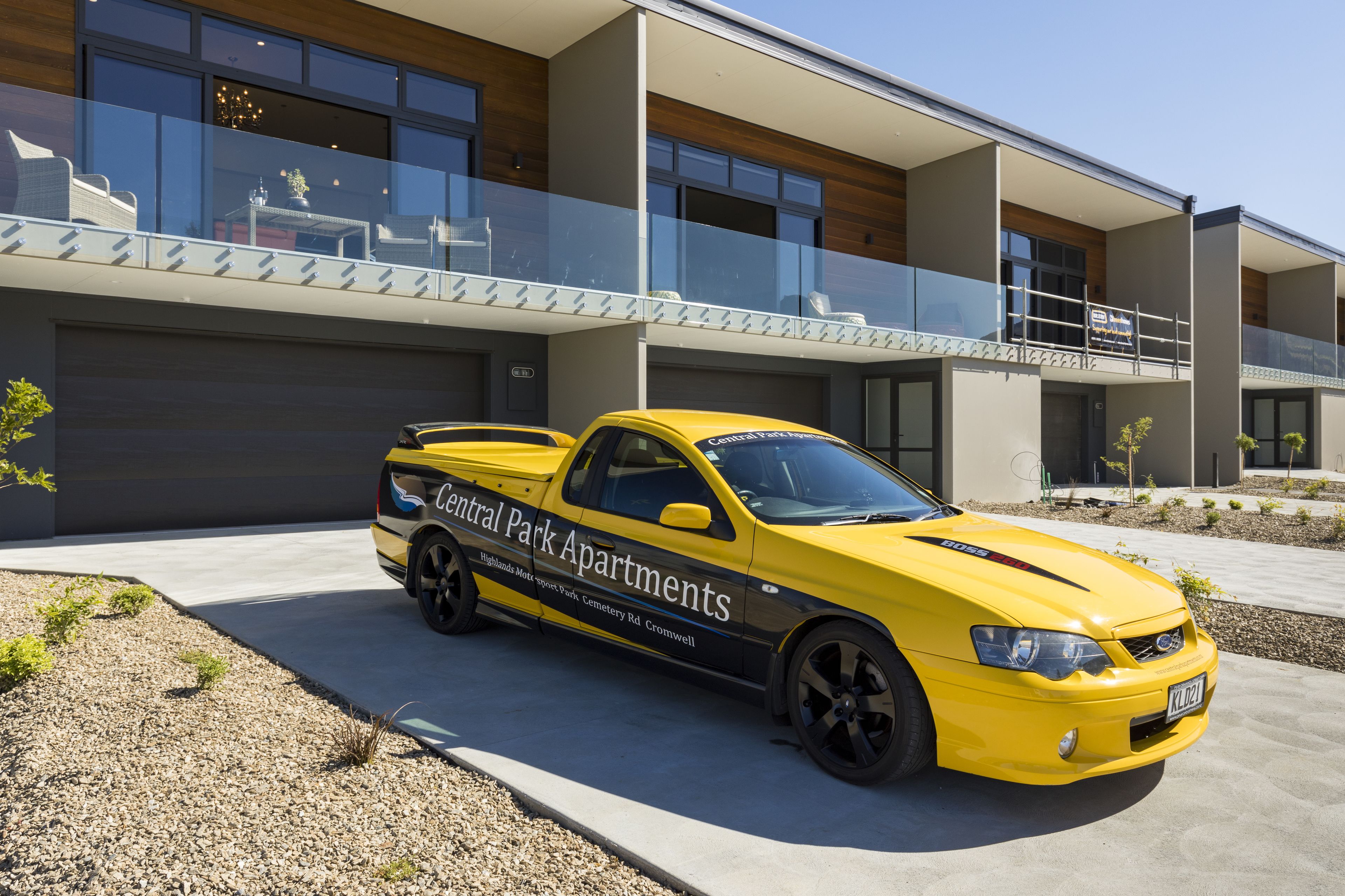 A yellow car parked in front of a modern building with a glass balcony.