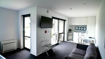 Una sala de estar moderna con un sofá, un televisor y una cocina visible a través de una puerta abierta.