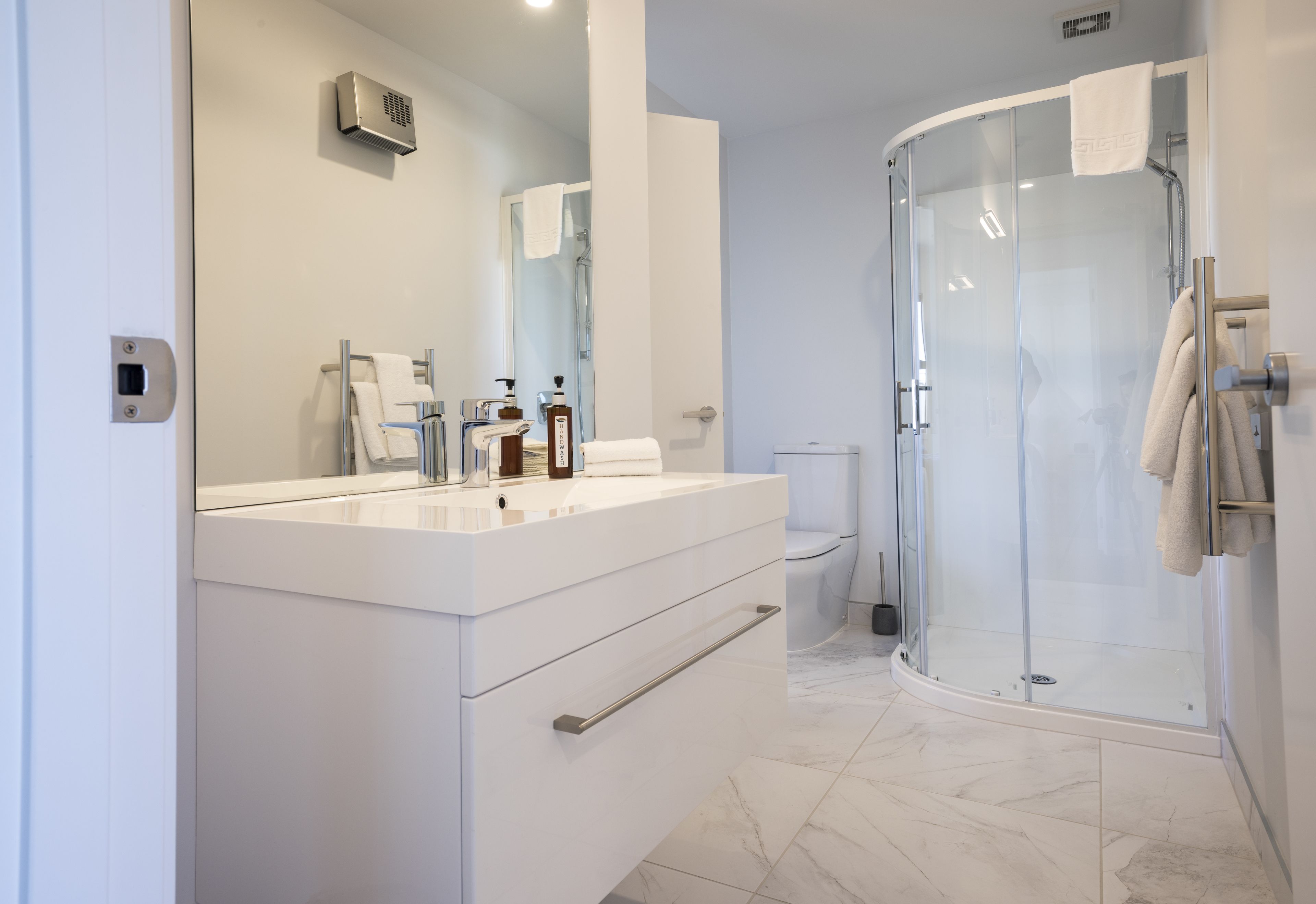 A modern bathroom with a white vanity, a glass shower enclosure, and a toilet.