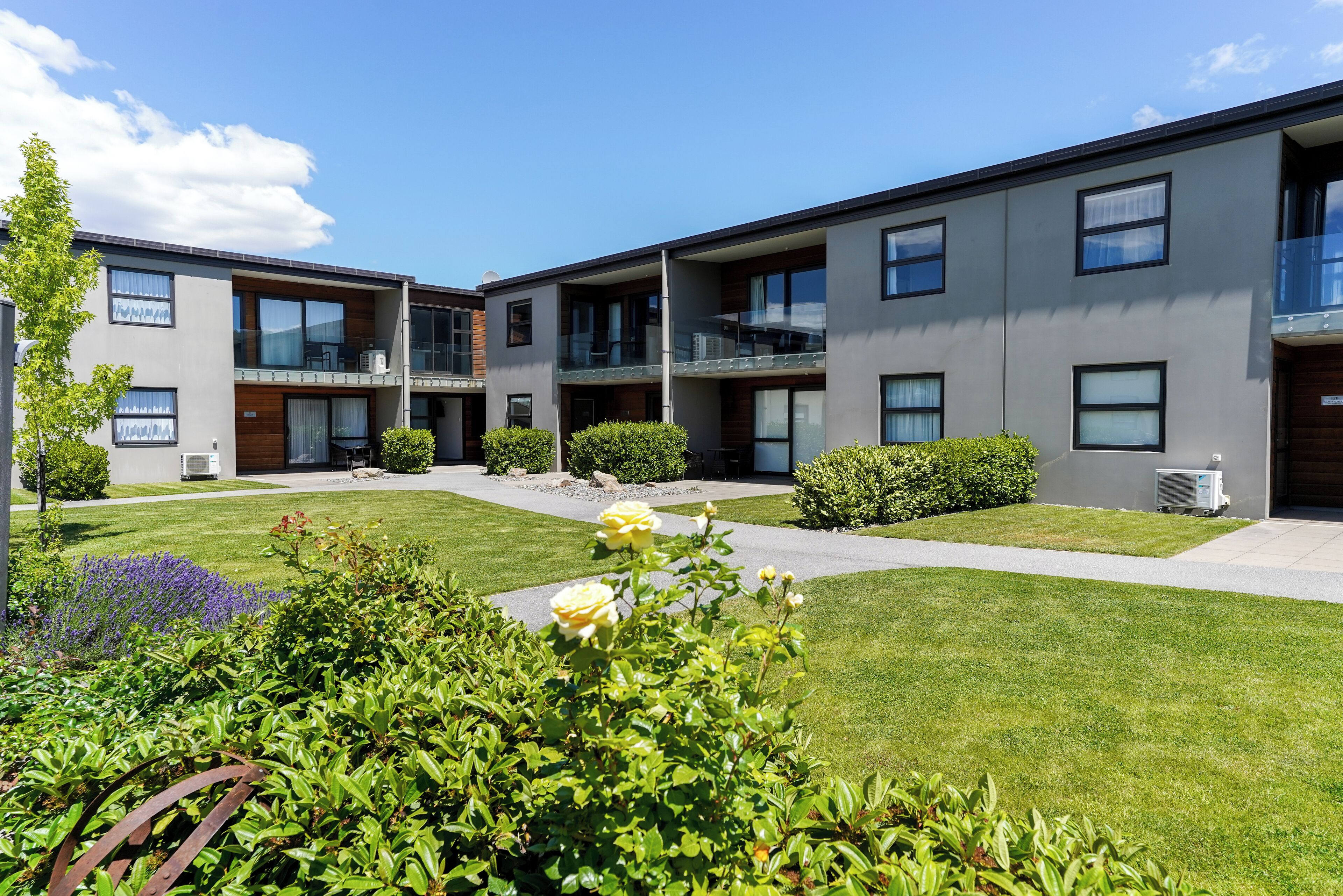 A modern building with multiple balconies and a well-maintained lawn with flowers.