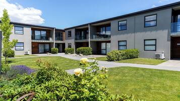 A modern building with multiple balconies and a well-maintained lawn with flowers.
