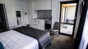 A hotel room with a bed, a desk with a chair, a kitchenette, and a balcony with a view.