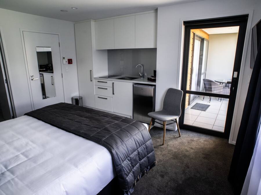 A hotel room with a bed, a desk with a chair, a kitchenette, and a balcony with a view.