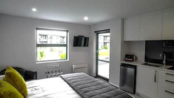 Una habitación pequeña con cama, televisión, ventana y kitchenette.