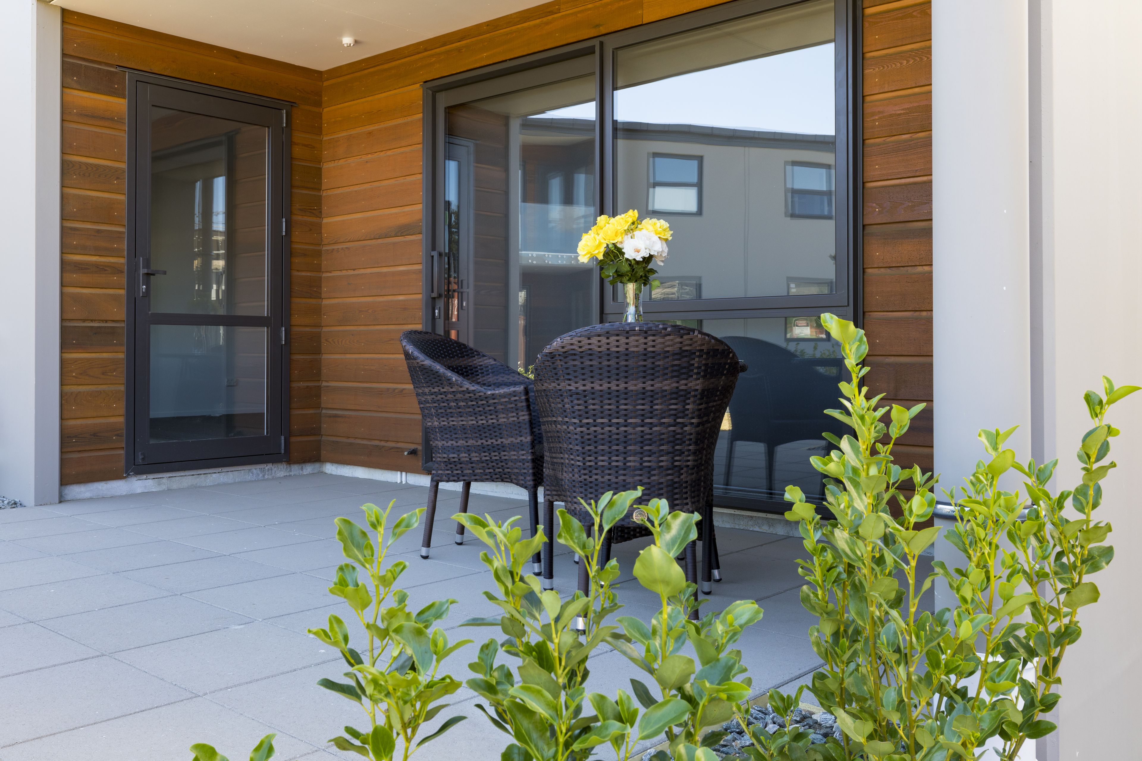Een modern zitgedeelte buiten, met rieten stoelen en een tafel, omgeven door potplanten.