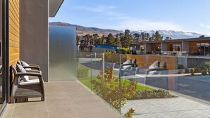 Un edificio moderno con un balcón de vidrio que da a un estacionamiento y un paisaje montañoso.