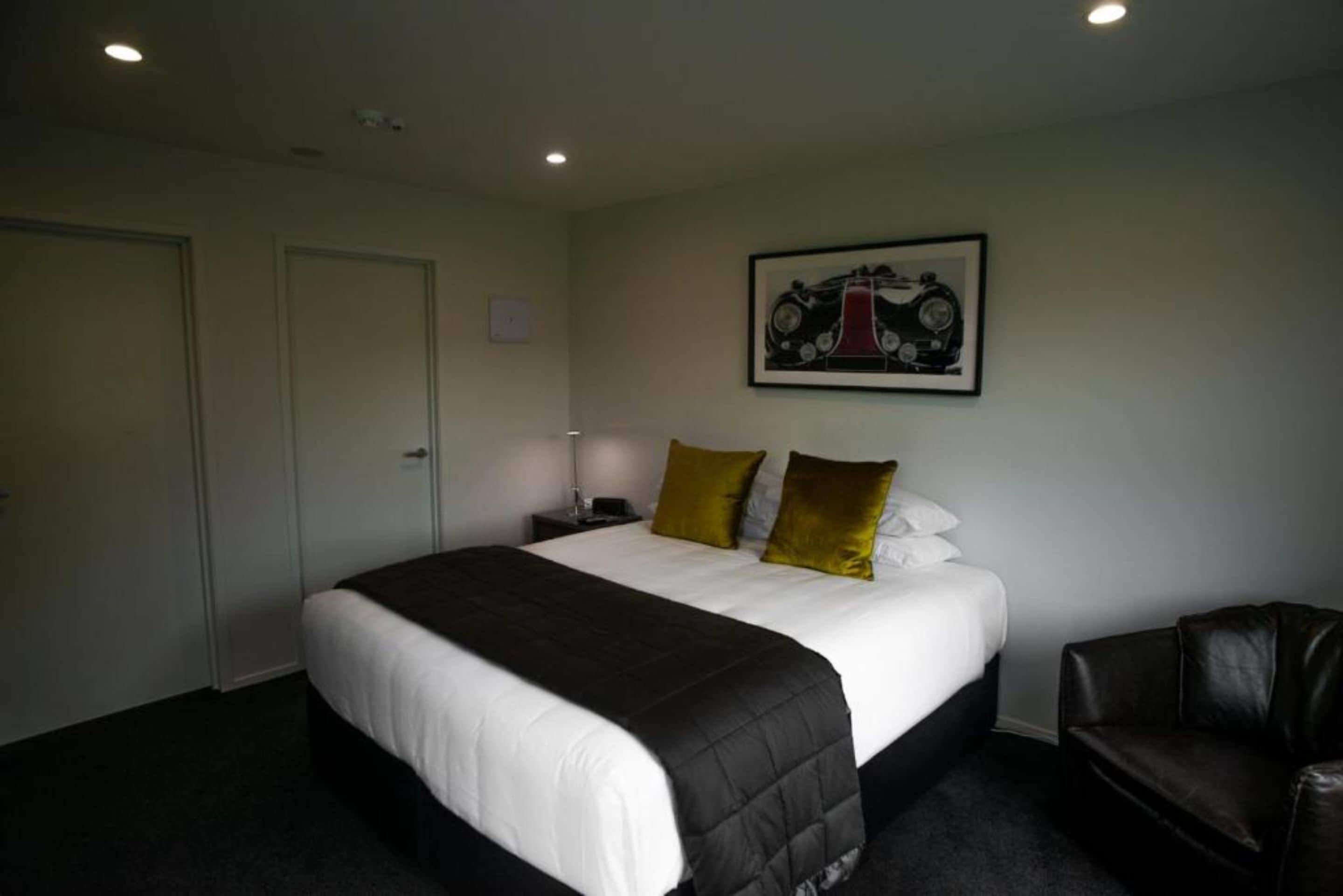 A hotel room with a large bed, a black leather chair, a nightstand, and a framed picture on the wall.