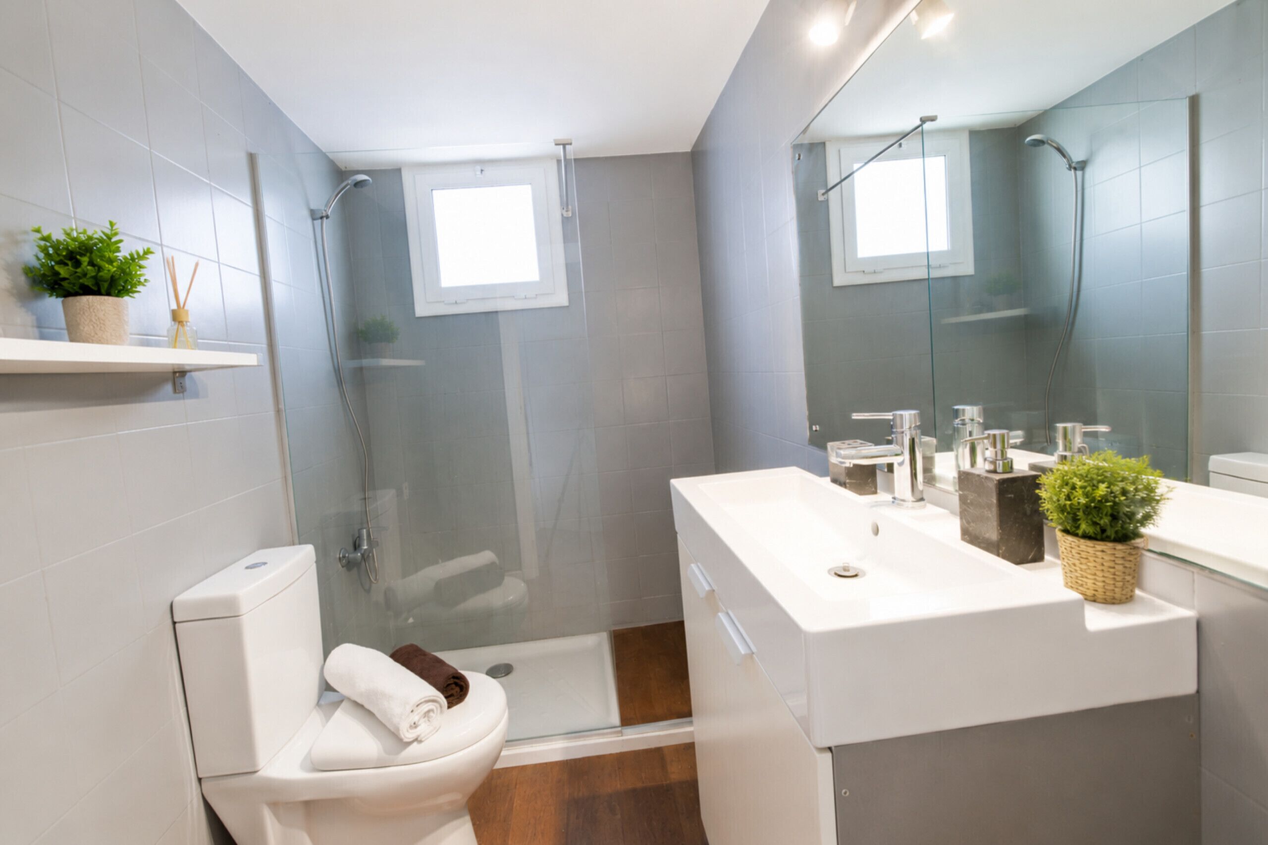 A modern bathroom with a glass shower enclosure, a white toilet, and a sink with a mirror above it.