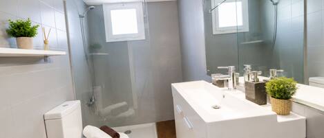 A modern bathroom with a glass shower enclosure, a white toilet, and a sink with a mirror above it.