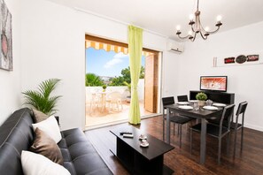 Un salon moderne comprenant un canapé, une table basse, une table à manger et des chaises. Une porte-fenêtre coulissante donne accès à un espace extérieur.