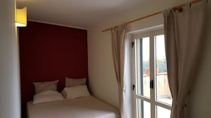 Un dormitorio con una cama, una ventana con cortinas y un aplique en la pared.