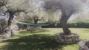 Una hamaca entre dos árboles en un jardín con macetas de piedra.