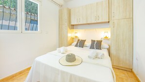 Una cama bien hecha con una colcha blanca, dos almohadas, un sombrero y toallas. Se ve una ventana con vistas a la vegetación.