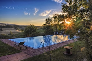 A rectangular outdoor swimming pool with a clear blue water surface, surrounded by a brick pathway and a grassy area.