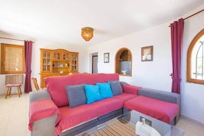 A living room with a red sofa, a wooden cabinet, and a chandelier. - Villa Cactus - PlusHolidays (Calpe)