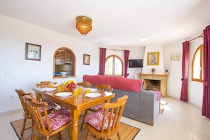 A dining area with a wooden table and chairs, a kitchen with a tiled backsplash, a fireplace, and a television mounted on the wall. - Villa Cactus - PlusHolidays (Calpe)