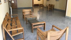 A spacious lobby with wooden chairs and tables, a reception desk, and framed artwork on the walls.