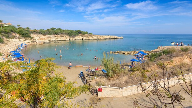 A beach with clear blue water, people swimming, and umbrellas.