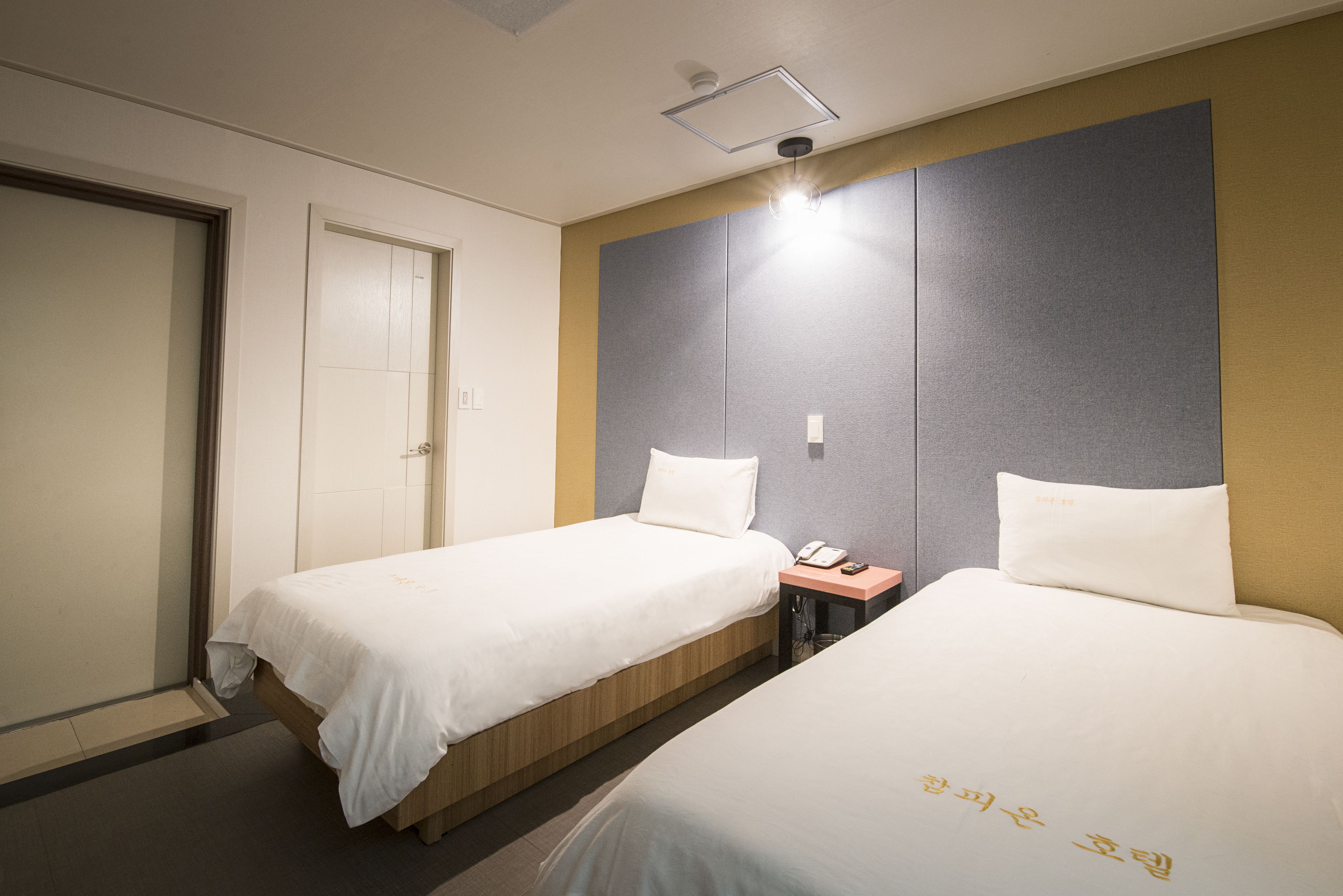 Una habitación de hotel con dos camas individuales, una mesita de noche con teléfono y una puerta.
