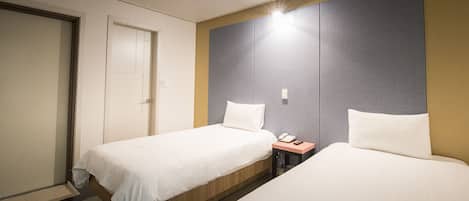 Una habitación de hotel con dos camas individuales, una mesita de noche con teléfono y una puerta.