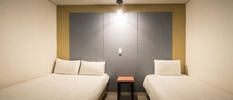 A hotel room with two single beds, a small table, and a light fixture above the bed.