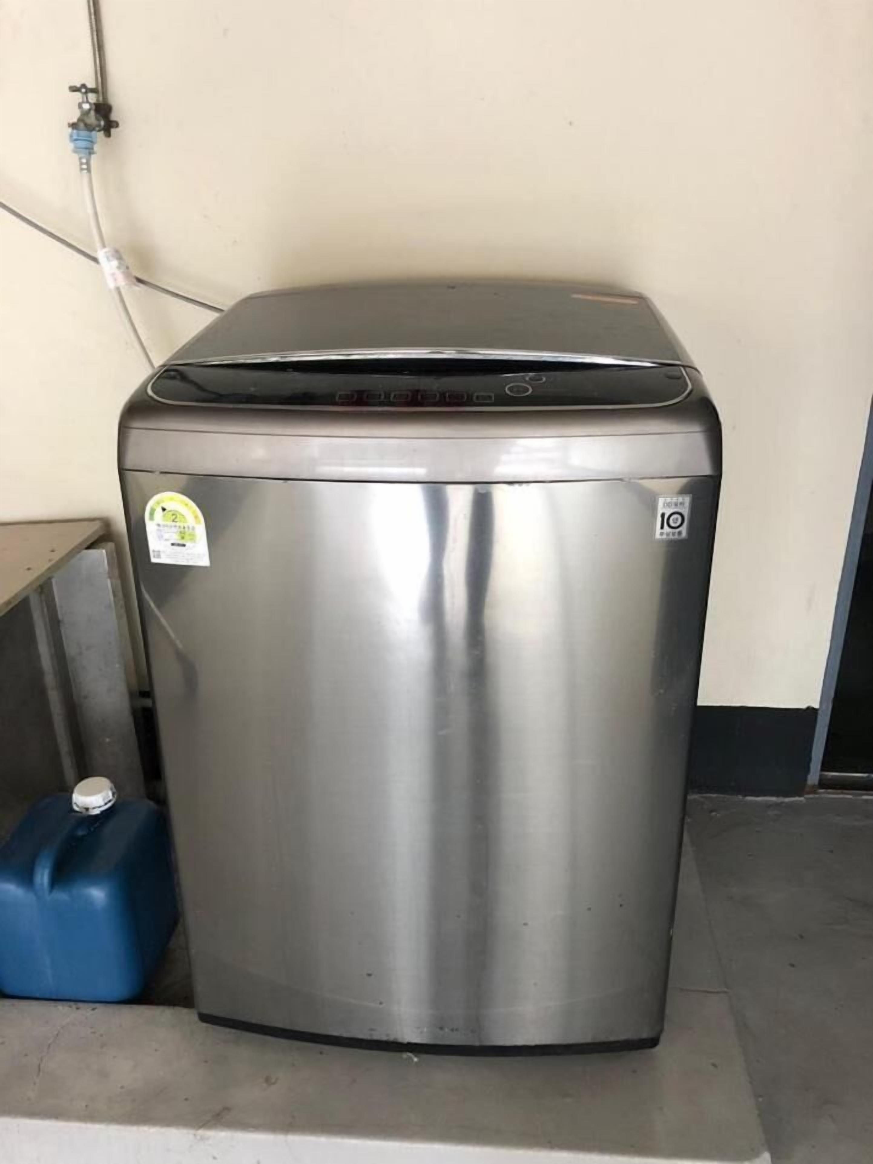Un cubo de basura pequeño de acero inoxidable con tapa, una botella de agua azul y un enchufe eléctrico fijado a la pared.