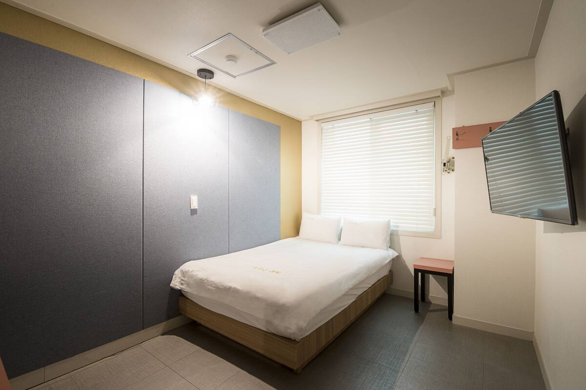 A bedroom with a bed, a desk, and a window with blinds.