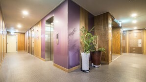A modern hotel corridor with a purple wall, wooden paneling, and a potted plant. - Champion Hotel Jeju (Jeju City)