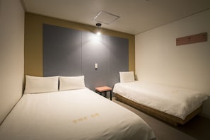 Quarto de hotel com duas camas de solteiro, uma mesinha e um nicho na parede.