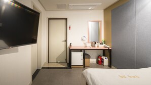 A hotel room with a bed, a desk with a mirror, a television, and a small refrigerator. - Champion Hotel Jeju (Jeju City)