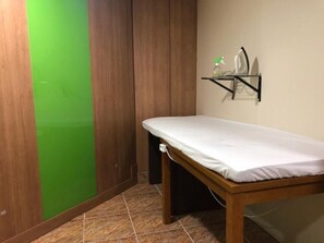 Una habitación pequeña y ordenada con una cama de madera, un separador verde y un estante con un atomizador y una plancha.