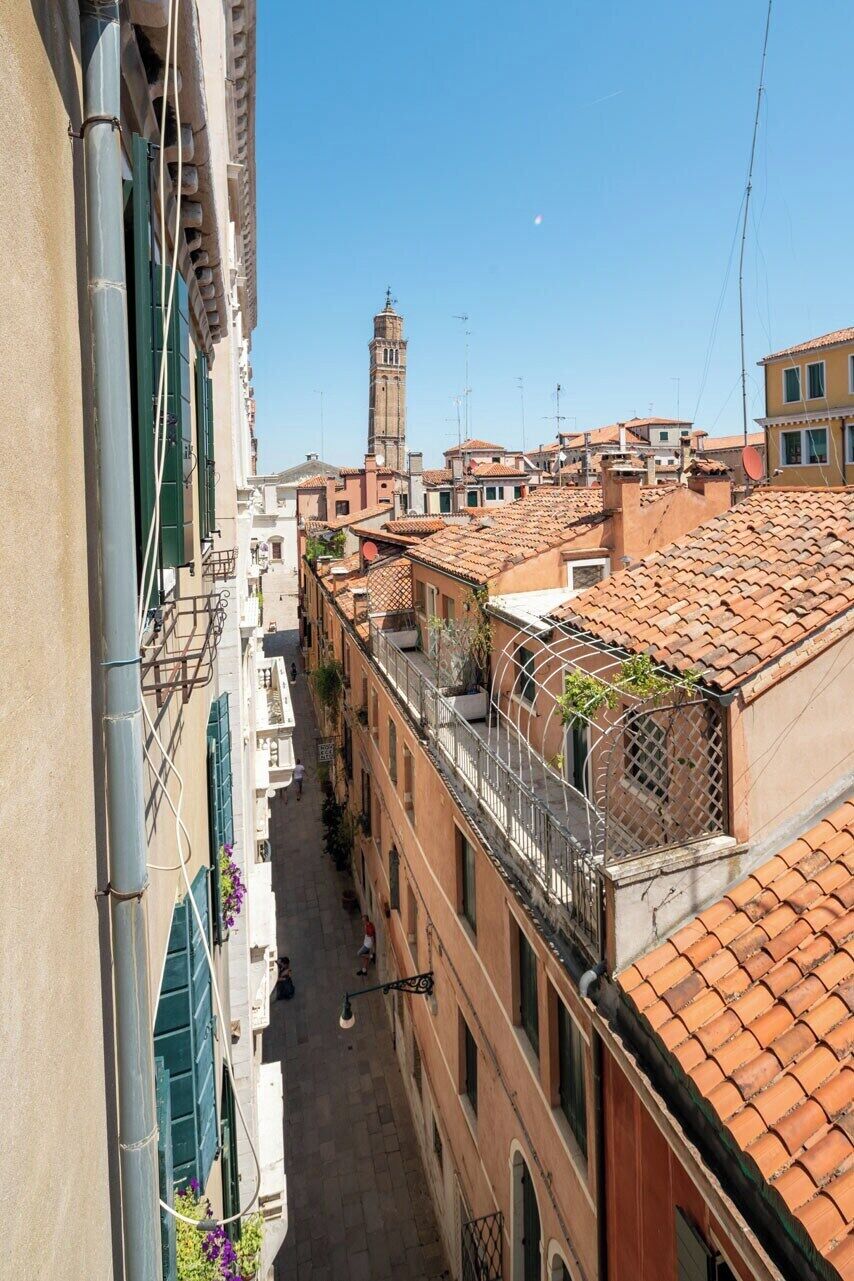A narrow street flanked by buildings with terracotta roofs and a prominent tower in the distance.