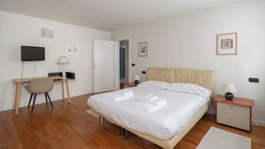 A bedroom with a bed, a desk, a chair, a television, and a door leading to another room.