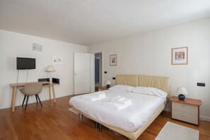 A bedroom with a bed, a desk, a chair, a television, and a door leading to another room.