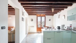 A kitchen with a central island, wooden beams on the ceiling, and a view to a balcony.