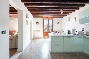 A kitchen with a central island, wooden beams on the ceiling, and a view to a balcony.