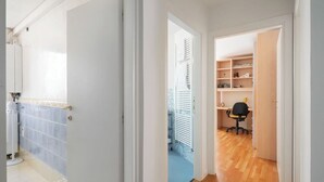 A hallway with a bathroom on the left, a kitchen area in the middle, and a room with a desk and chair on the right.