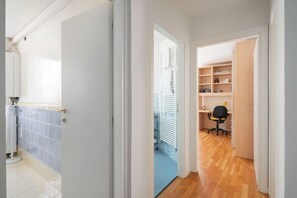 A hallway with a bathroom on the left, a kitchen area in the middle, and a room with a desk and chair on the right.