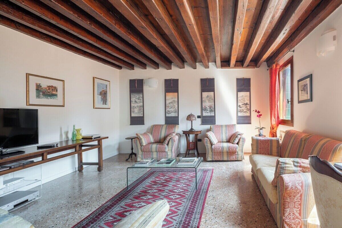 A living room with wooden beams, a flat-screen TV, striped sofas, and a patterned rug.