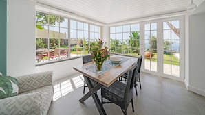 A bright, open dining area with a wooden table, black wicker chairs, and a view of a garden through large windows. - Funchal Character Villa, Seaview | Quinta Alegria (Funchal)