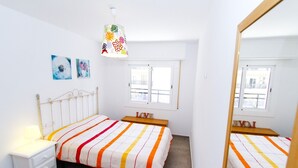 A bedroom with two beds, a nightstand, a mirror, and a window.
