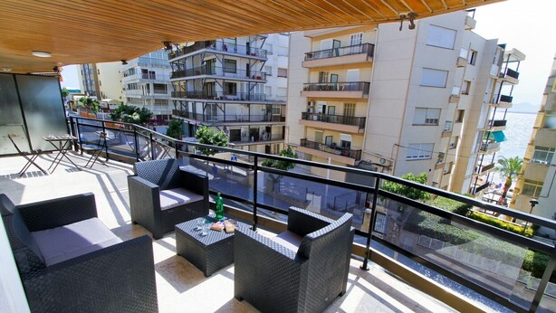 A balcony with outdoor furniture, a view of adjacent buildings, and a clear sky.