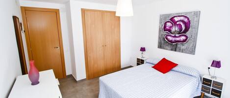 A bedroom with a bed, a bedside table, a lamp, a painting, and a wardrobe.
