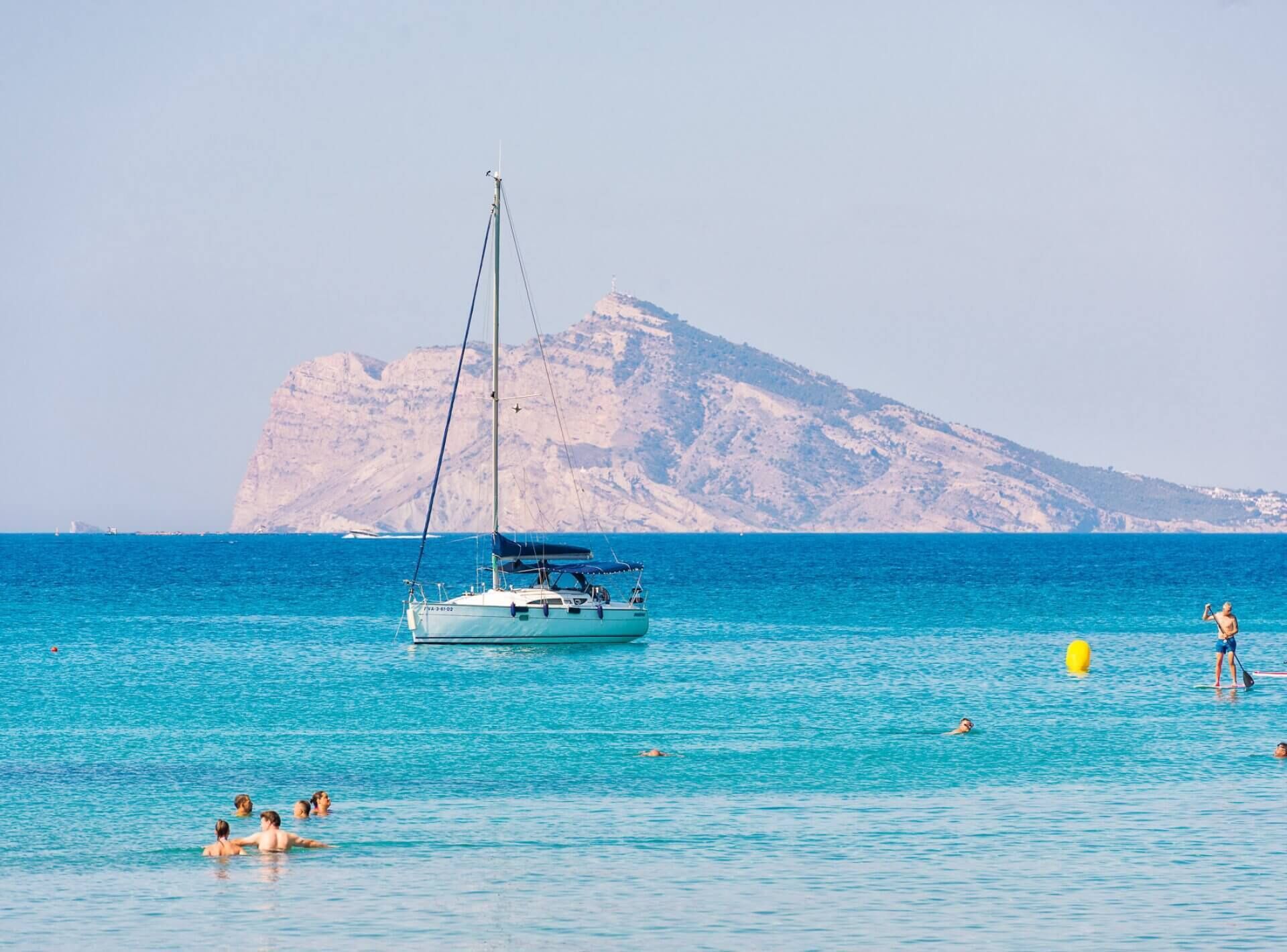 A sailboat on calm waters with a mountainous backdrop.
