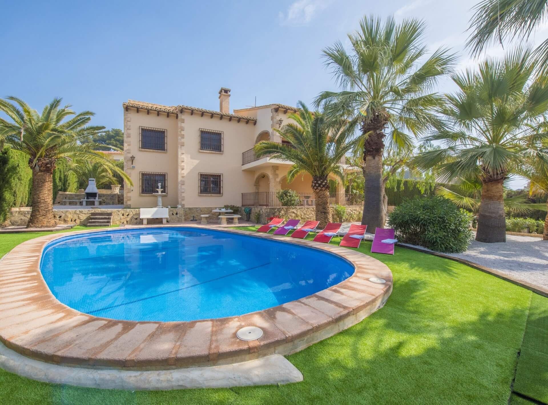 Una piscina de borde curvo, rodeada de césped cuidado y palmeras.