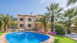 A swimming pool with a curved edge, surrounded by a well-maintained lawn and palm trees.